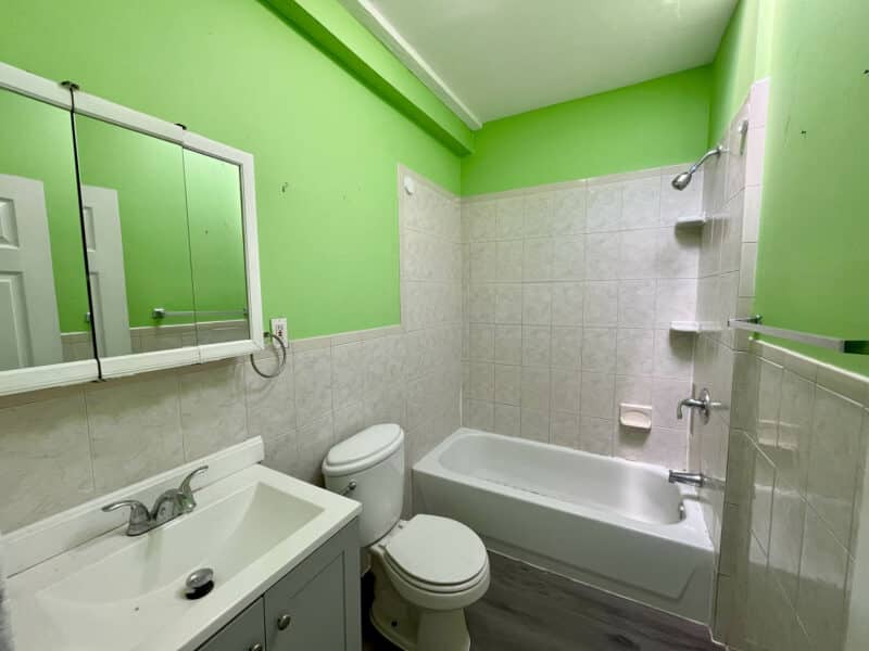 Full bathroom with bathtub, shower, vanity sink, and green accent walls in Baltimore townhome at 2115 E. Federal Street.