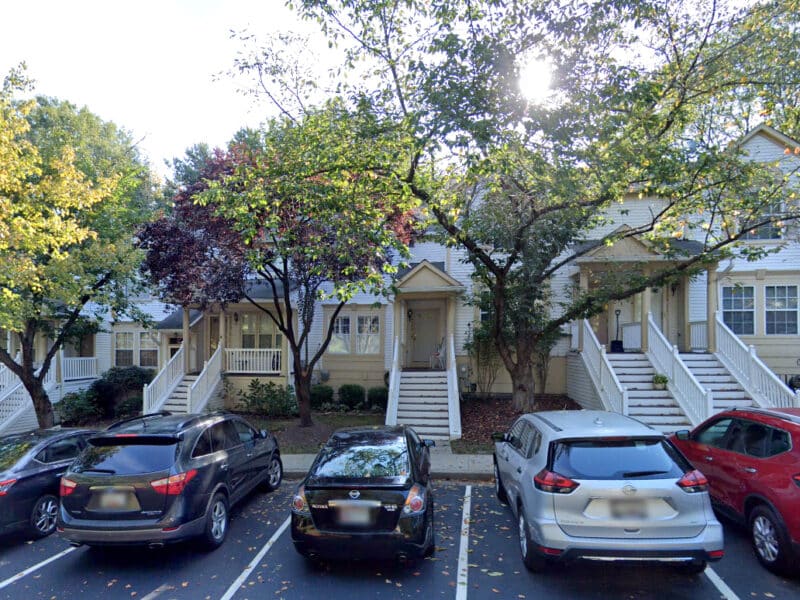 Exterior view of townhouses with trees and cars in the foreground.