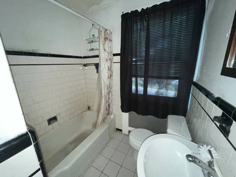 Full bathroom with ceramic tile flooring, tub/shower combo, and black-and-white wall tile.