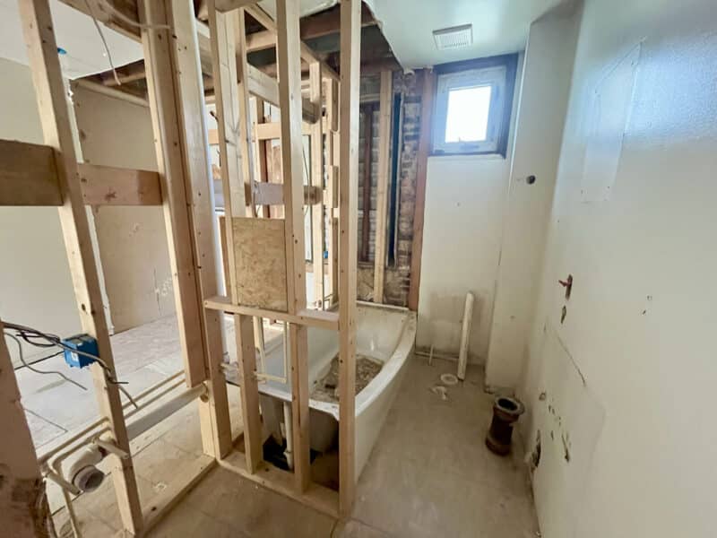 Bathroom under construction with clawfoot tub, framed walls, and plumbing rough-ins.