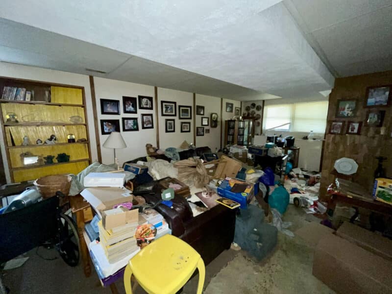 Cluttered living area at 2009 Halethorpe Avenue in Halethorpe Terrace, Baltimore County, with carpet flooring, paneled accent wall, shelving, and windows.