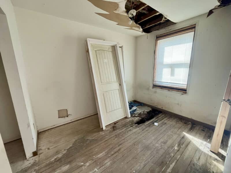 Upper-level room with hardwood floor, window, and damaged ceiling section.