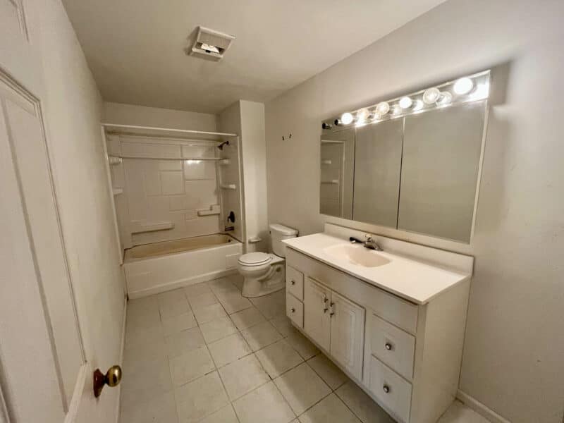 Full bathroom with long vanity, tiled flooring, and mirror lighting.
