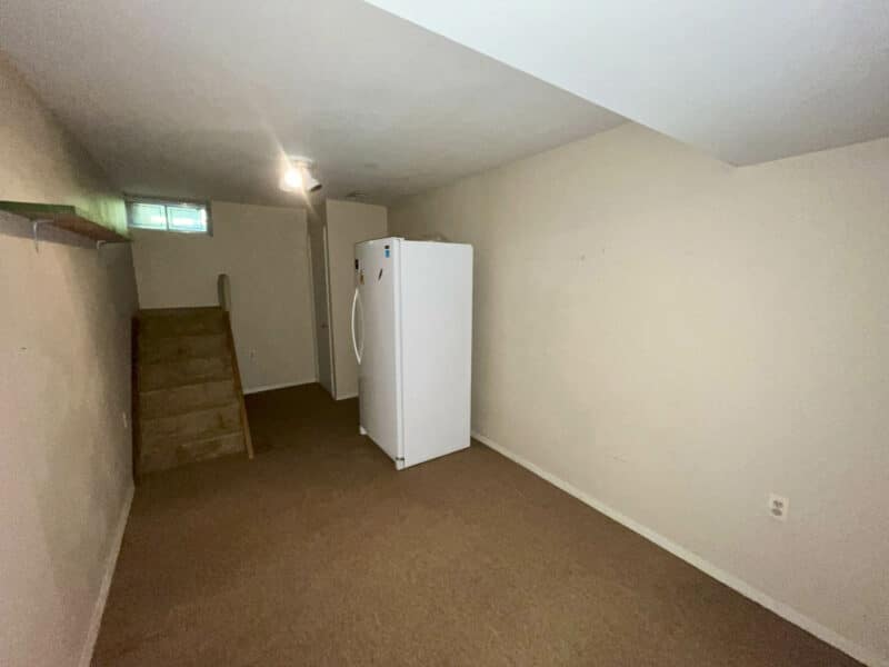 Basement room with carpet flooring, refrigerator, and stair access in Westminster ranch home