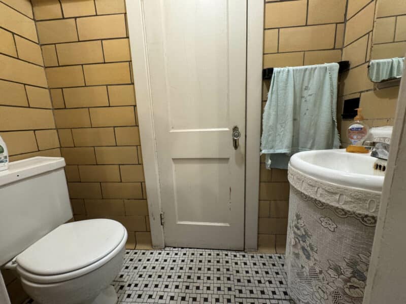Small bathroom with yellow tile walls, patterned floor, and pedestal sink.