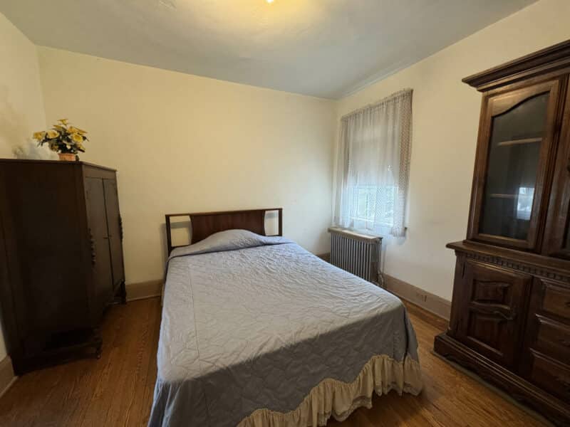 Bedroom with bed, hardwood floors, radiator, and large wooden wardrobe.