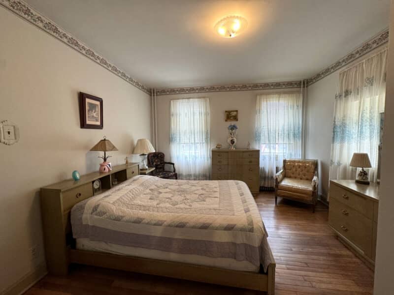 Bedroom with large bed, dresser set, hardwood floors, and patterned wallpaper border.