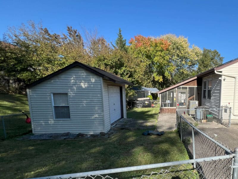 Detached garage with siding and roll-up door behind fenced backyard in Westminster, Maryland.