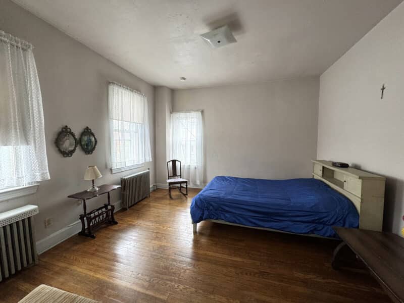 Large bedroom with hardwood floors and windows with sheer curtains.