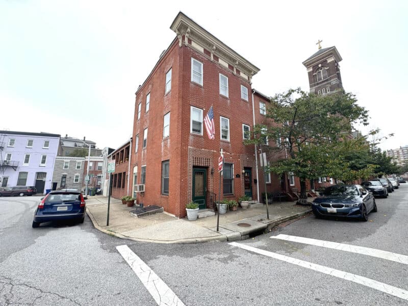 Corner exterior of brick rowhome with sidewalk and trees.