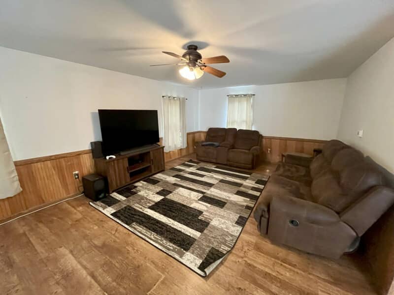 Living room with wood paneling, ceiling fan, recliners, and area rug