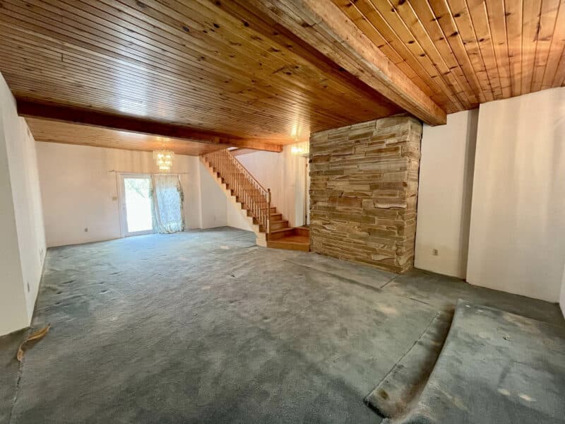 Living room with wood-paneled ceiling, stone accent wall, and open staircase.