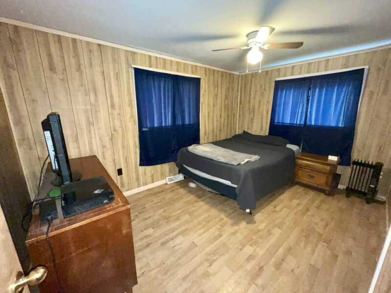 Bedroom with double windows, wood paneling, and ceiling fan