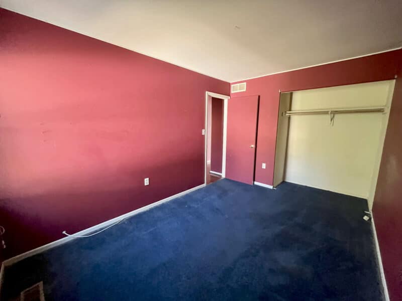 Bedroom with deep red accent wall, blue carpet flooring, and closet space in Westminster rancher