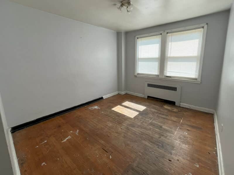 Bright bedroom with hardwood floors, gray-painted walls, and large windows.