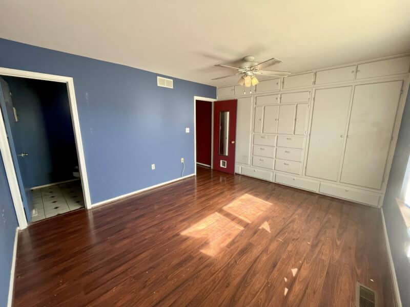 Primary bedroom with hardwood flooring, blue accent wall, ceiling fan, and large built-in closet in Westminster rancher.