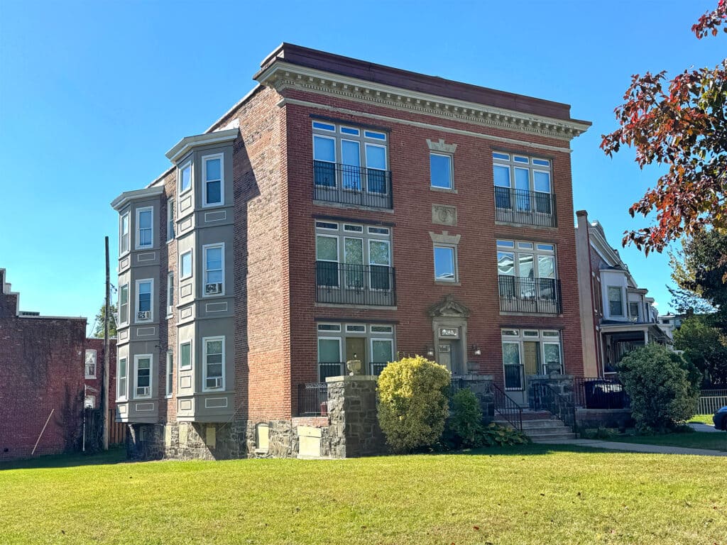 Stately three-story brick apartment building at 901 Chauncey Avenue in Reservoir Hill, shown from a left-side angle with manicured lawn and mature landscaping.