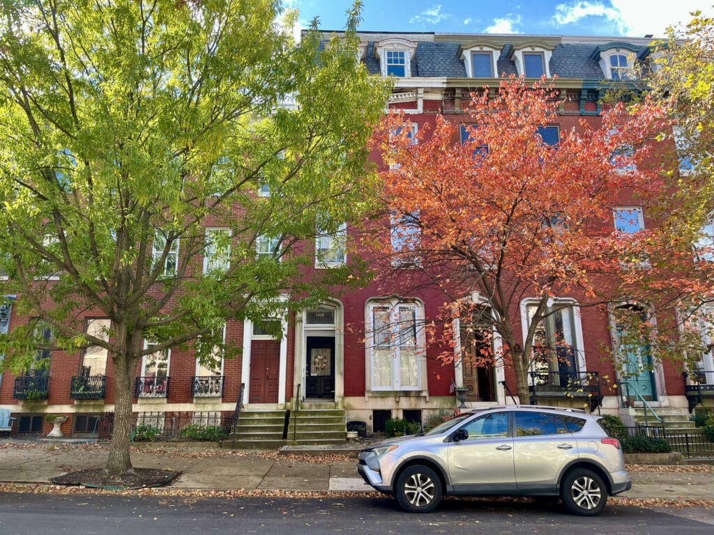 Historic red-brick multi-unit building at 1416 Park Avenue in Bolton Hill, framed by mature trees with fall foliage.