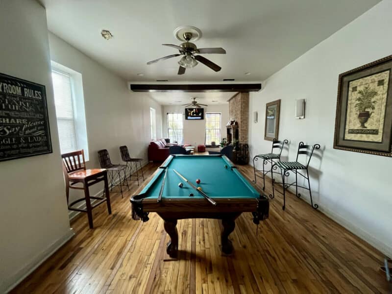 Pool table centered in open room with seating and ceiling fan.