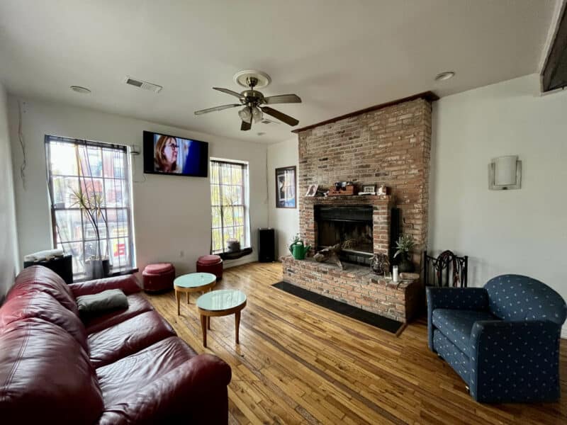 Living room featuring red brick fireplace, wood floors, and natural light from multiple windows.