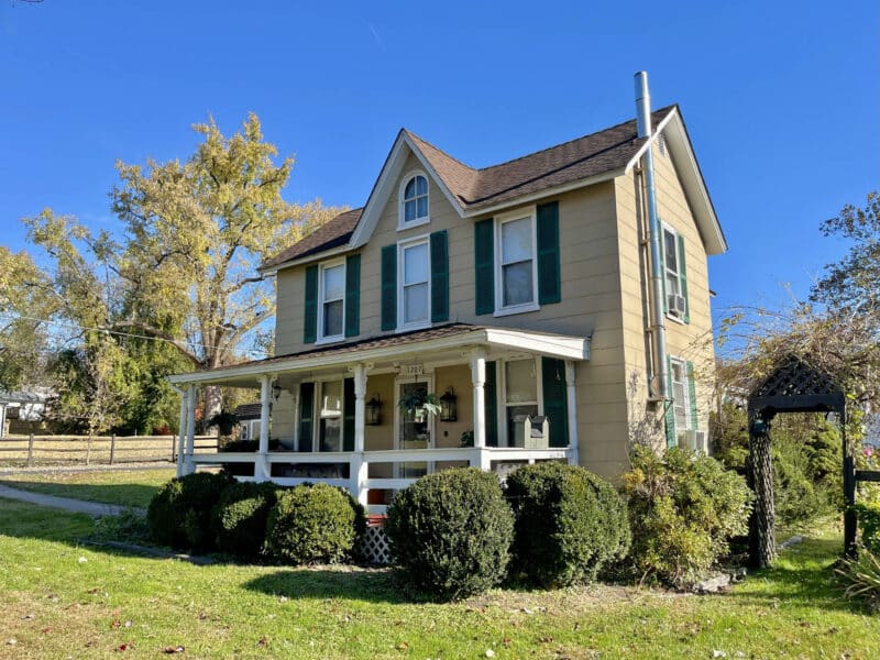 Front exterior of two-story farmhouse at 1207 Joppa Road in Joppa, Maryland, showing porchfront design, mature landscaping, and fenced yard.