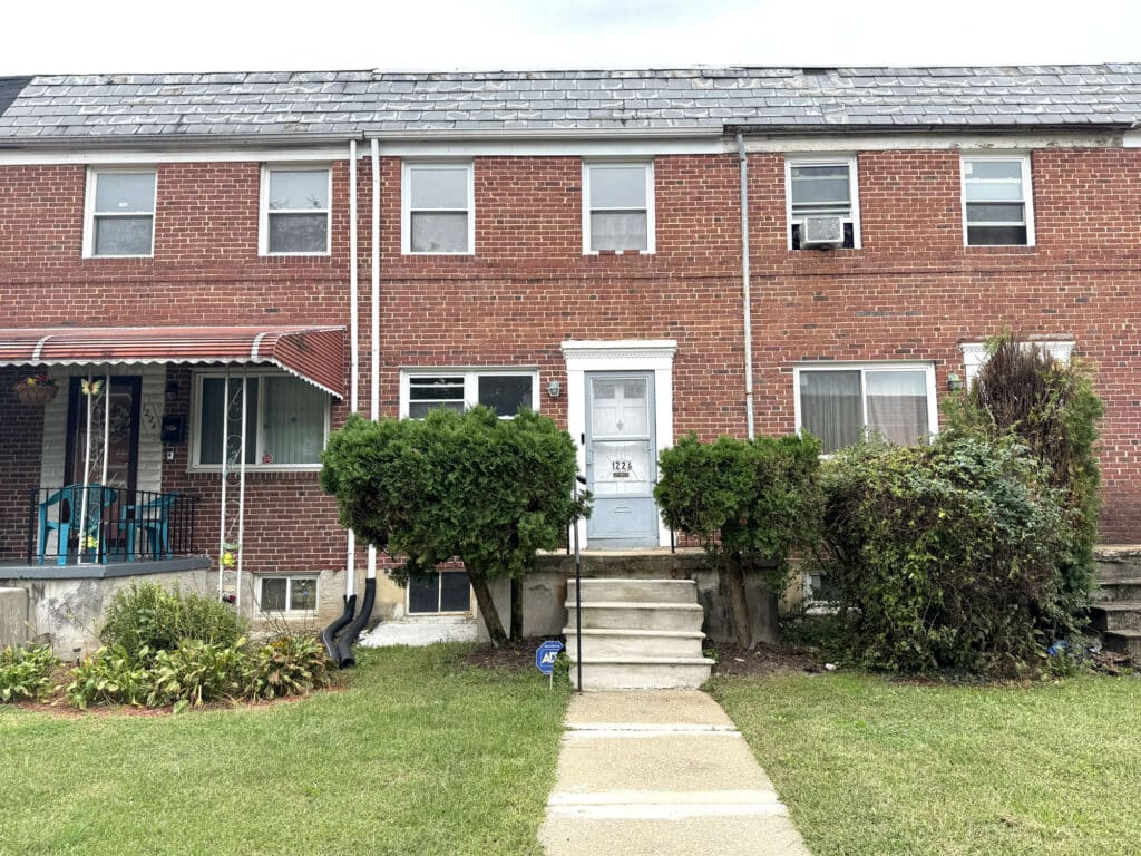 Brick two-story townhome with front steps, shrubs, and small lawn.