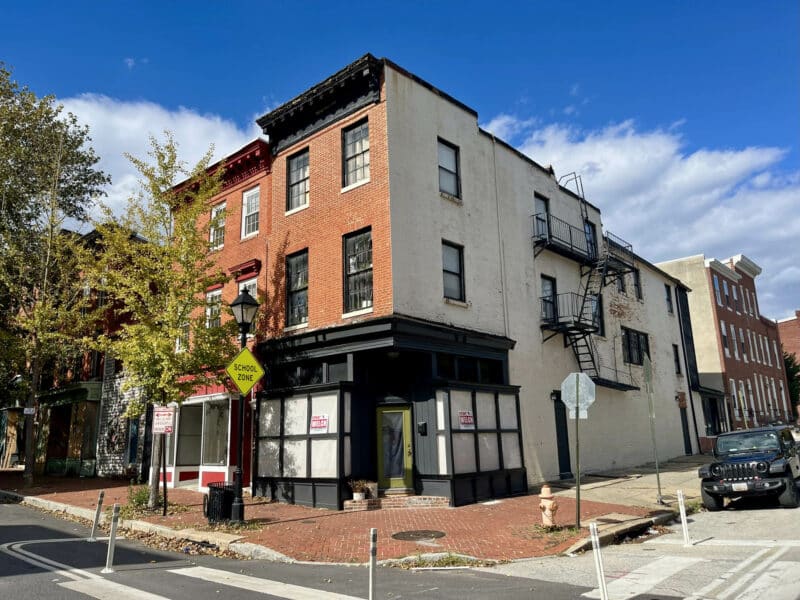 Three-story end-of-group brick storefront building at 1500 W. Baltimore Street on the corner of N. Stricker Street in the Franklin Square neighborhood.