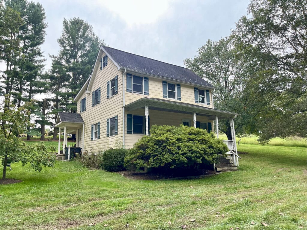 Front exterior of two-story farmhouse in Hydes, Maryland with covered porch and mature landscaping.