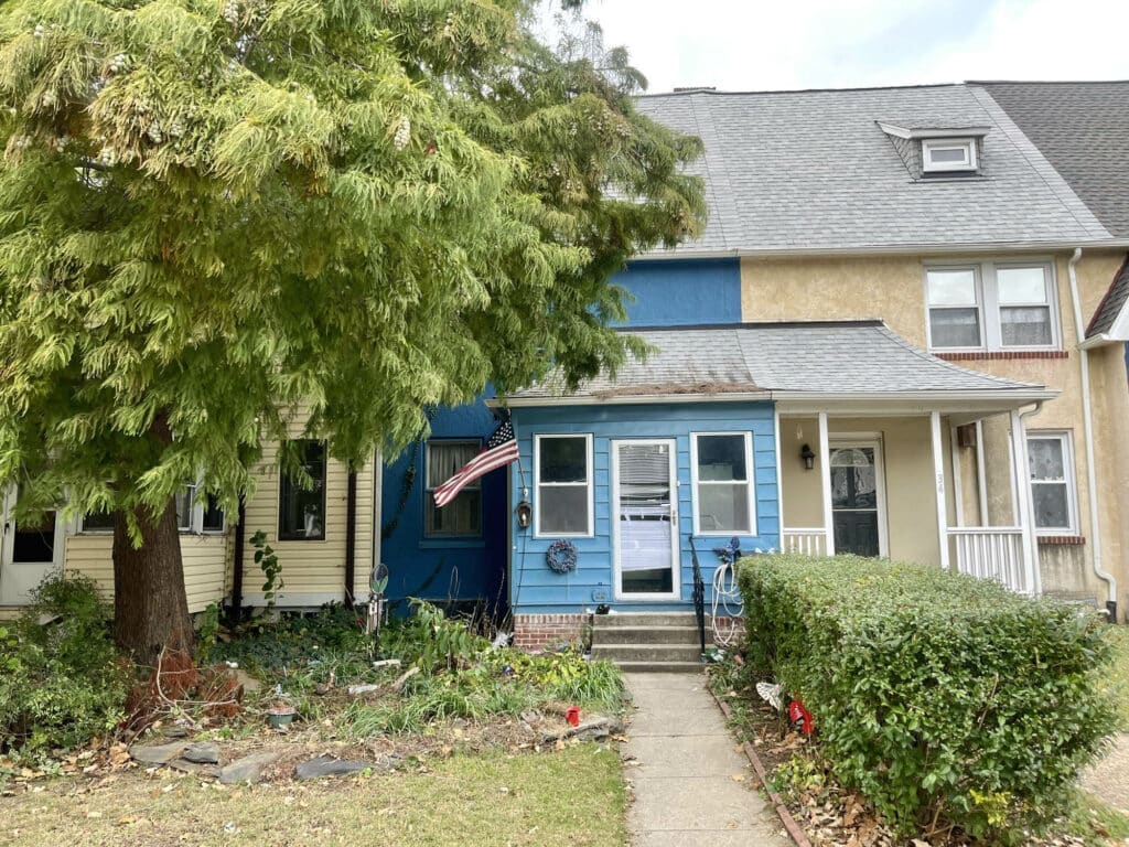 Front exterior of blue two-story townhome with enclosed porch and mature tree.