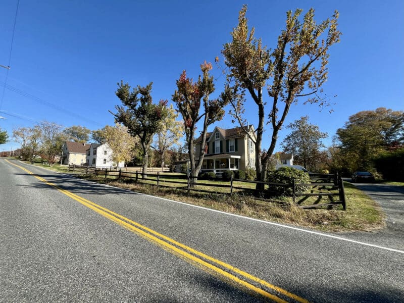 Wide-angle exterior view of 1207 Joppa Road in Joppa, Maryland, showing two-story farmhouse, front porch, mature landscaping, and paved driveway.