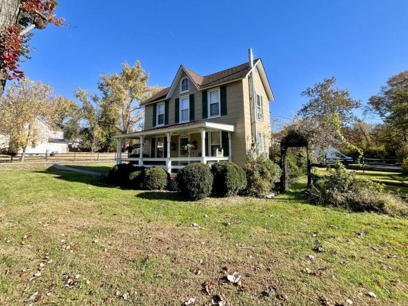 Front exterior of two-story farmhouse at 1207 Joppa Road in Joppa, Maryland, showing porchfront design, mature landscaping, and fenced yard.