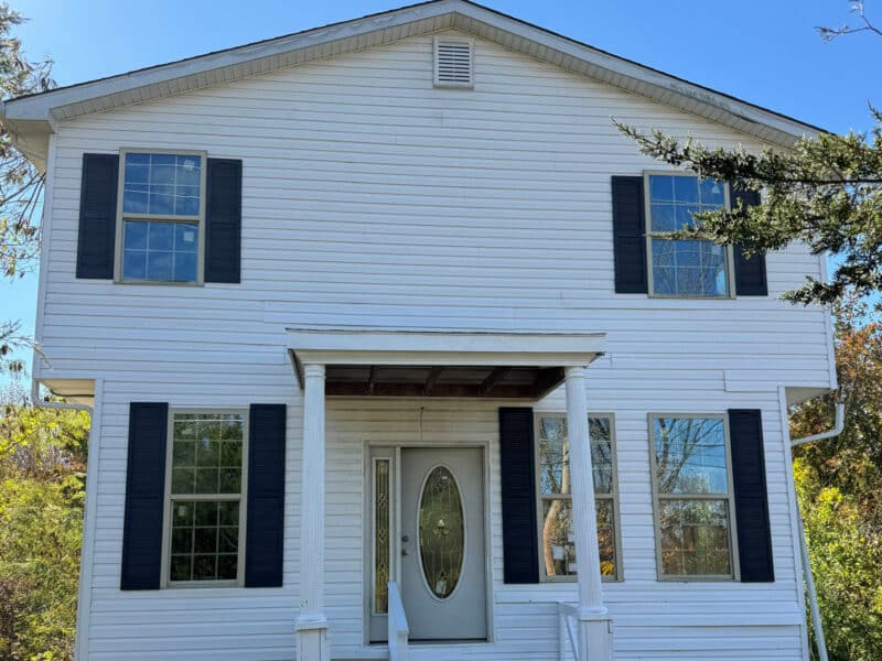 Front elevation of white two-story home with black shutters and oval glass entry door.