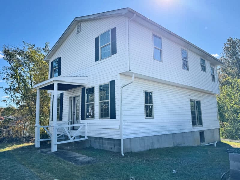 Two-story detached home with covered front porch, black shutters, and unfinished interior on a large grassy lot in Huntingtown, Maryland.