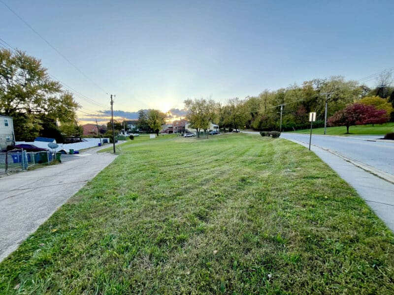 Ground-level view of the open residential lot at 4611 Bowleys Lane, showing clear grassed area with homes and trees in the background.