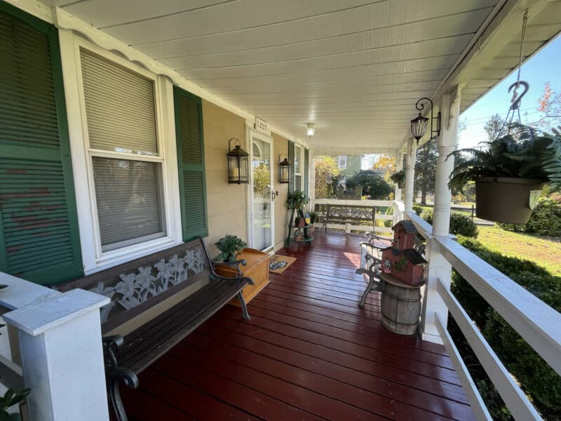 “Front porch of the two-story farmhouse at 1207 Joppa Road in Joppa, Maryland, featuring covered entry, railing, and mature landscaping.