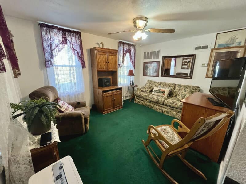 Front living room of 1207 Joppa Road farmhouse with green carpeting, front windows, and neutral interior.