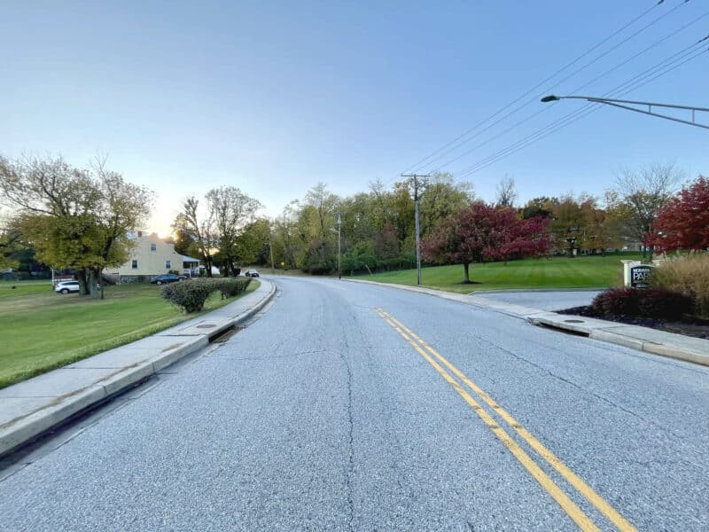 View of Bowleys Lane looking toward trees and landscaped areas near Herring Run Park, with sidewalks and road frontage visible.