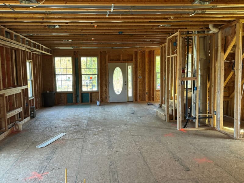 Interior framing showing open floor plan with exposed studs, subflooring, and new construction work.