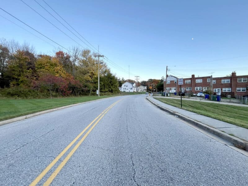 View of Bowleys Lane facing residential rowhomes and open grassy areas near the 0.323-acre lot.