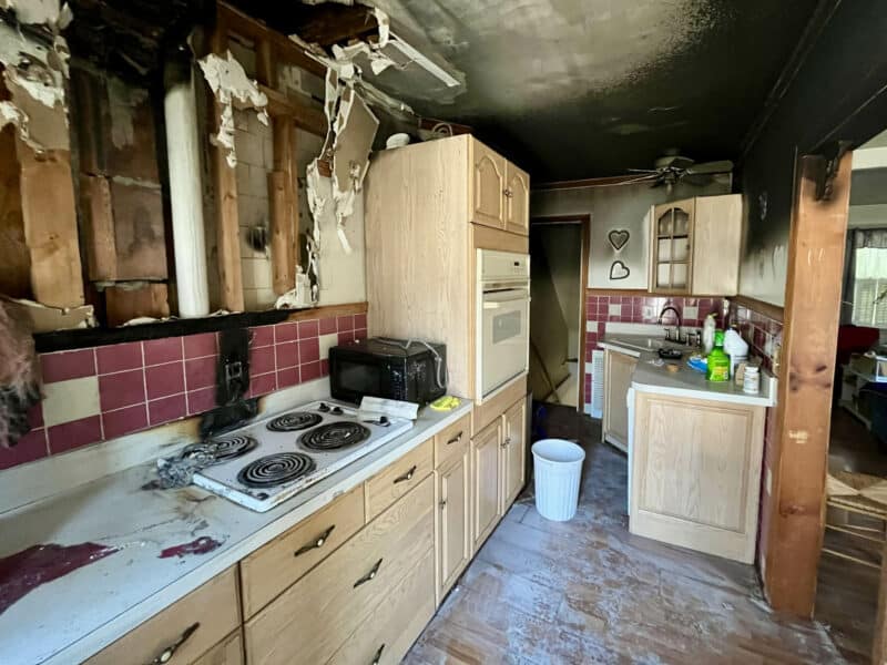 View of damaged kitchen with burned cabinets, tiled backsplash, and electric cooktop.