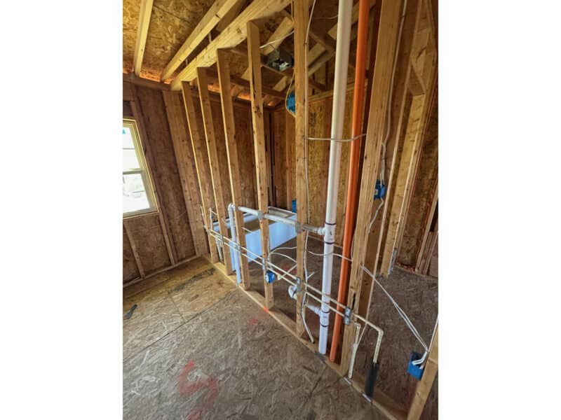 Second-floor plumbing rough-ins with new pipes and venting installed between studs.