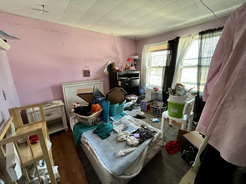 Bedroom with pink walls, clutter, and personal belongings.