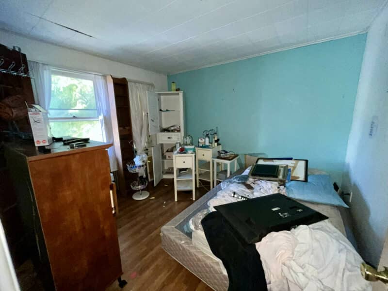 Bedroom with blue walls, scattered items, and hardwood flooring.