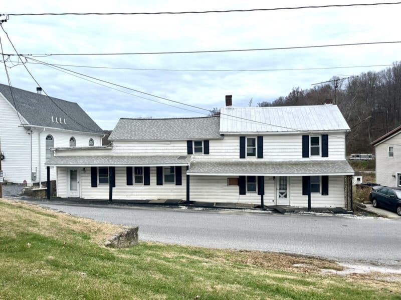 Two-story gutted and framed home in Finksburg, Maryland, shown from the street with a long covered porch and off-street parking.