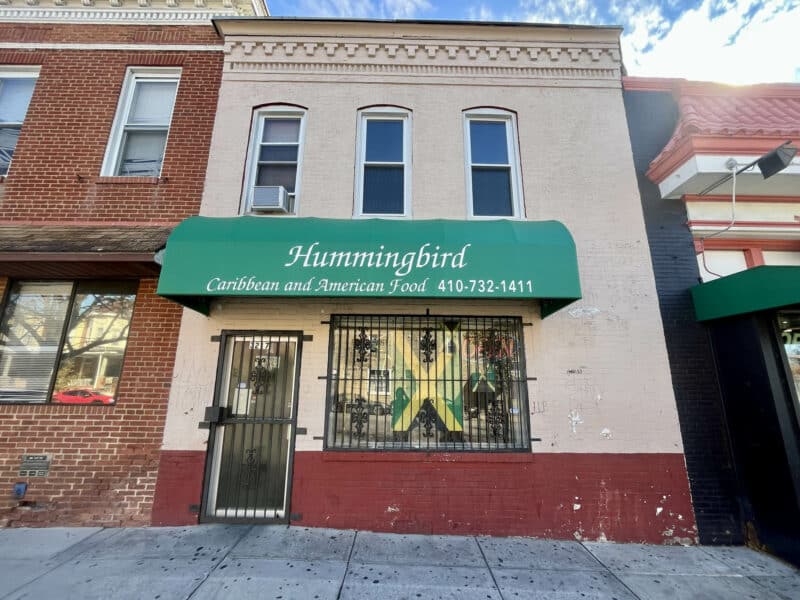 Front exterior of 3217 Belair Road, brick commercial building with green awning for Hummingbird Carryout along Belair Road commercial corridor in Northeast Baltimore.