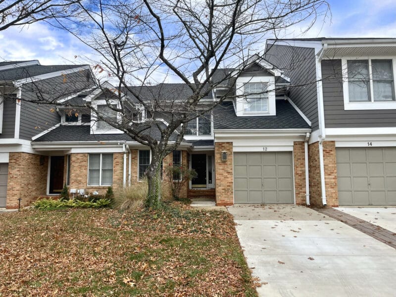 Front view of townhome showing brick façade, siding accents, front lawn, and attached garage.