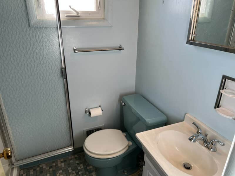 Bathroom featuring blue toilet, walk-in shower with frosted glass door, white vanity, and mosaic floor tile.