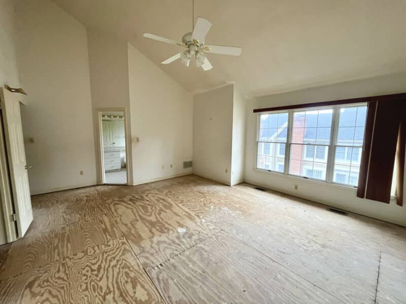 Large primary bedroom with vaulted ceiling, ceiling fan, oversized window, and unfinished subfloor.