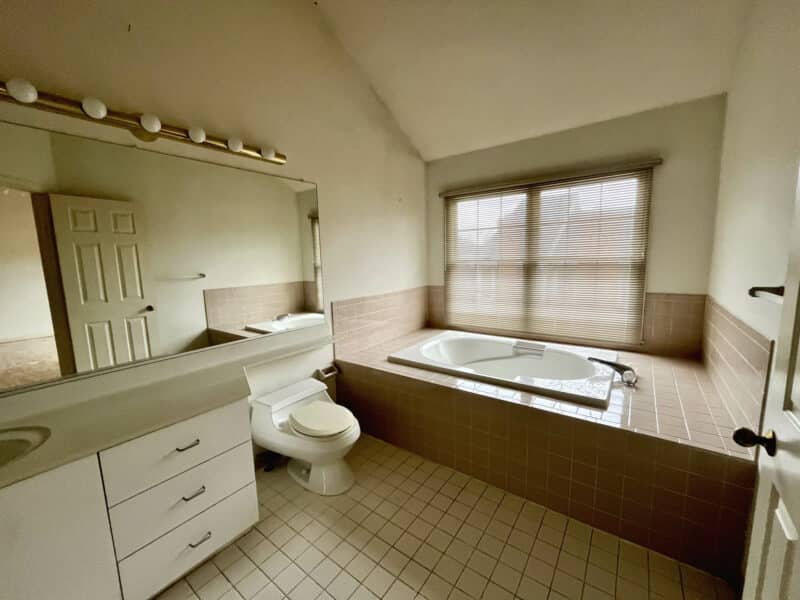 Primary bathroom featuring a large soaking tub with tile surround, single vanity, and window with blinds.