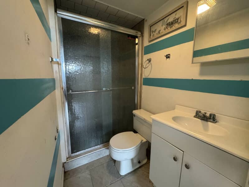 Bathroom with tiled flooring, shower with sliding glass doors, white vanity cabinet, and striped teal wall accents inside two-story townhome at 2808 Windsor Avenue in West Baltimore.